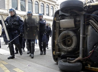 Riot police officers walks by an overturned car during a students demonstration in Lyon today.