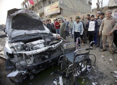 People inspect a destroyed car and a wheelchair at the scene of a car bomb attack Baghdad, Iraq, today.
