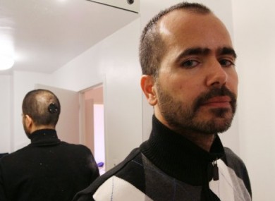 With the back of his head reflected in a mirror, artist Wafaa Bilal poses for a photograph.