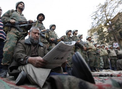 A protester reads a newspaper as he sits before a line of Egyptian Army soldiers in Tahrir Square, Cairo, today.