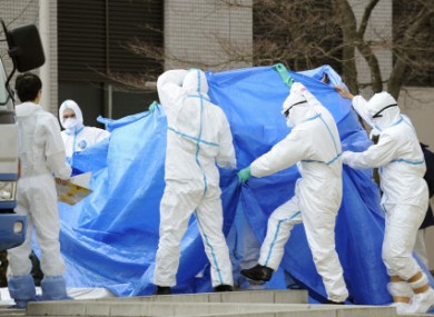 A man who had been working to restore power and cooling functions at the Fukushima Daiichi nuclear plant walks to a special vehicle for radioactive decontamination, while being shielded with a blue sheet to conceal his identity