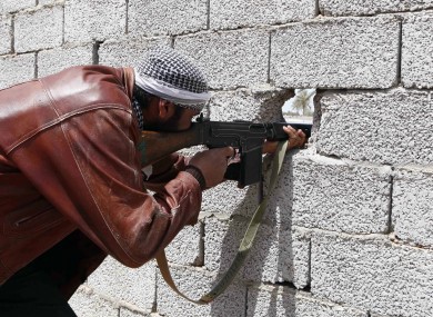A Libyan rebel fighter fires his weapon through a hole in a wall during battle with pro-Gadhafi troops in the besieged city of Misrata.