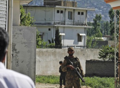 A Pakistan army soldier secures a street in front of the house in which Osama bin Laden was killed (background).