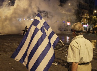 An elderly man holds the Greek flag as tear gas billows in Athens yesterday