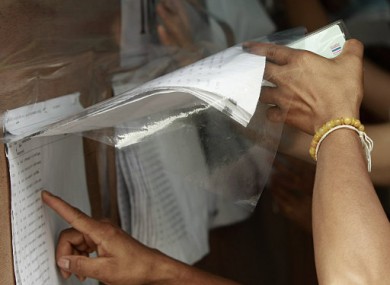 Holding an ID card in one hand, a Thai citizen browses lists of voters before casting absentee vote at a stadium in Bangkok, Thailand, Sunday, June 26,