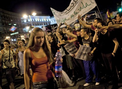 A Catholic pilgrim walks past shouting protesters in Madrid