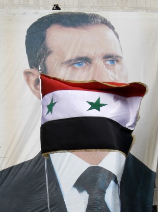 A Syrian flag flies as pro-Syrian regime protesters hold a rally in support of President Bashar Assad, pictured in the large banner, in Damascus, Syria today.