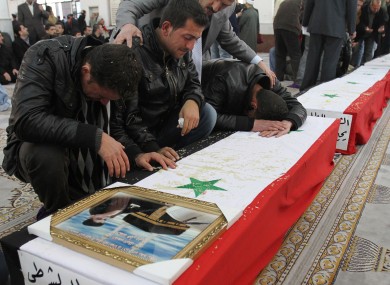 Syrian men mourn over the coffin of one of 11 Syrian police officers who were killed in an explosion in the Midan neighborhood on Friday