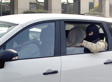 An unidentified man with his head covered, believed to be Abdelkader Merah or his companion, sits between masked police officers as they head to the French police's anti-terrorist headquarters