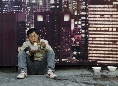 A migrant worker has a meal in front of a billboard advertising a real estate project in Shanghai.