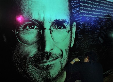 A man writes a message on a board erected in dedication to Steve Jobs following his passing