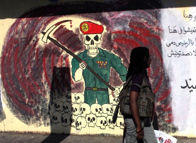 An woman passes by a wall with graffiti depicting the ruling military council and Arabic that reads,