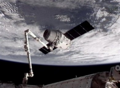 This image provided by NASA-TV shows the SpaceX Dragon commercial cargo craft, top, after it was grabbed by a robotic arm at the ISS.