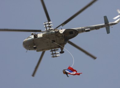 A Syrian regime supporter dangles from a helicopter as he waves Russian and Chinese flags