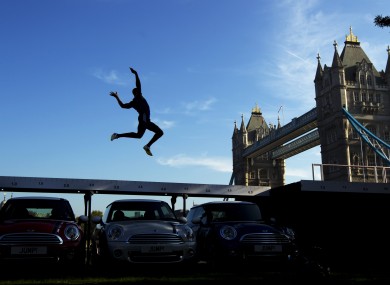 Current British long jump champion J.J. Jegede is silhouetted as he performs an exhibition jump over three Mini cars backdropped by Tower Bridge in London