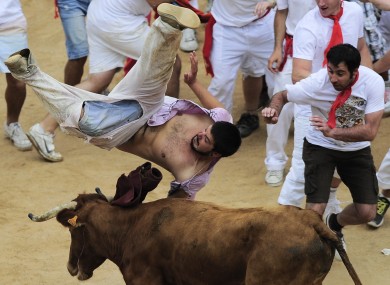 A reveler is tossed by a cow in the bull ring, at the end of third running of the bulls at the San Fermin fiestas, in Pamplona, Monday, July 9, 2012