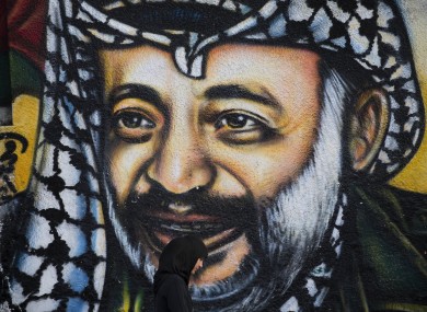 A Palestinian woman walks past a graffiti depicting late Palestinian leader Yasser Arafat in Gaza City.