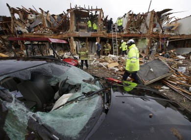 A smashed car sits in front of an apartment complex destroyed by an explosion at a fertiliser plant in West, Texas, as firefighters conduct a search and rescue mission.