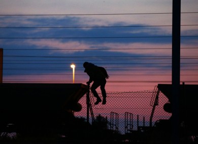 A migrant climbing the fence on to the tracks at the Eurotunnel site