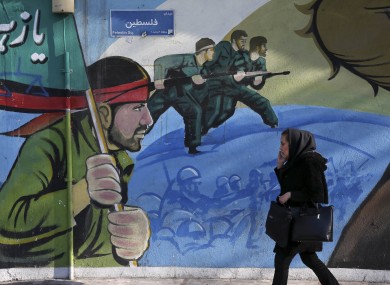 An Iranian woman walks past a mural depicting Iranian armed forces in the battlefield, at Palestine Square.