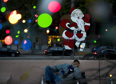 Homeless man Alonzo Harrison, 47, takes a nap on a bench at Pershing Square decorated with Christmas lights in the background in LA.