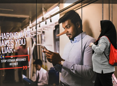 A commuter walks past an advertisement reading 'sharing a lie makes u a liar' at a train station in downtown Kuala Lumpur.