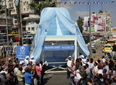 Palestinians applaud in front of a symbolic chair supporting the Palestinian statehood bid in the West Bank city of Ramallah, unveiled Tuesday, Sept. 20, 2011.