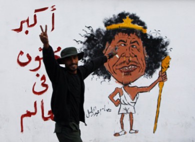A Libyan man gestures front of a graffiti reading: