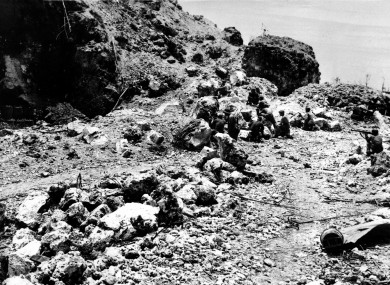 US Marines crouch behind rocks before the entrance to a cave where Japanese soldiers were holed up, during the invasion at Peleliu island in the Palau group on 10 October 1944.