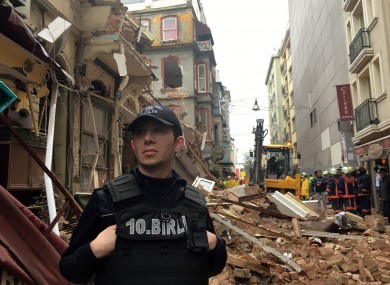 A police officer stands near the collapsed building as firefighters investigate.