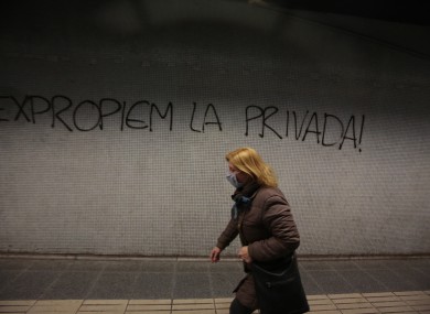 A woman wearing protective mask walks past a graffiti message reading 'Expropriate the private (hospitals and clinics)' inside a train in Barcelona, Spain.