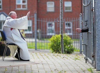 Fr McCafferty hearing confessions while observing social distancing though the locked gates of Corpus Christi Church