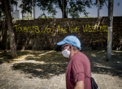 A man walks past graffiti reading 'tourists you are not welcome' on a wall of Barcelona's La Barceloneta district.