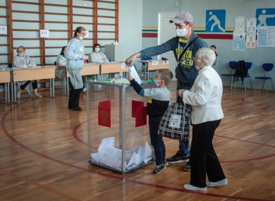 A young child helps his father place his vote in a ballot box at a polling station in Russia.