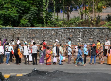 People wearing face masks stand in a queue outside a NESCO vaccination centre in Mumbai.