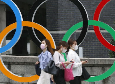 People wearing face masks walk past the Olympics Rings statue in Tokyo