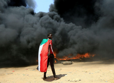 A person wearing a Sudan's flag stand in front of a burning pile of tyres during a protest against prospect of military rule in Khartoum, Sudan.