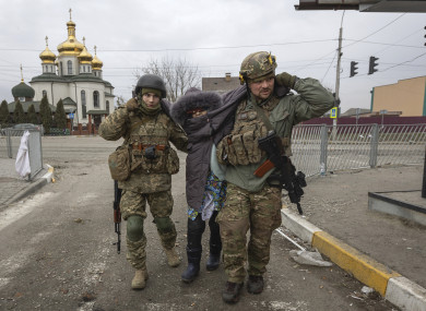 Ukrainian servicemen help an elderly woman in the town of Irpin on Sunday.