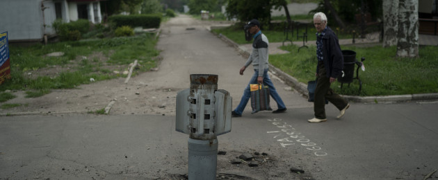 People walk past part of a rocket that sits wedged in the ground in Lysychansk.